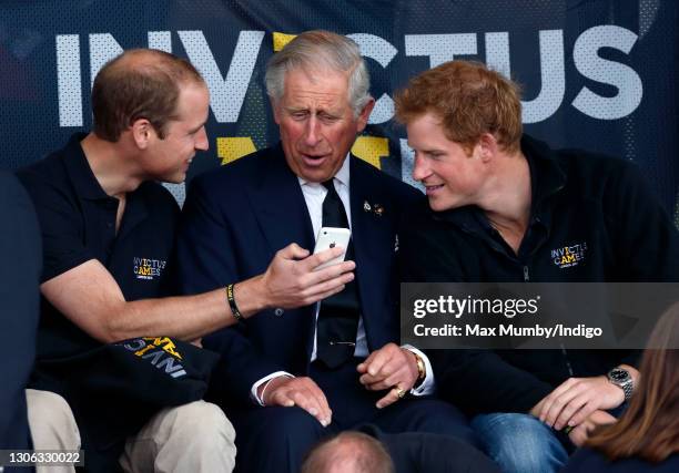 Prince William, Duke of Cambridge, Prince Charles, Prince of Wales & Prince Harry look at an Apple iPhone as they watch the athletics during the...