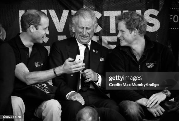 Prince William, Duke of Cambridge, Prince Charles, Prince of Wales & Prince Harry look at an Apple iPhone as they watch the athletics during the...