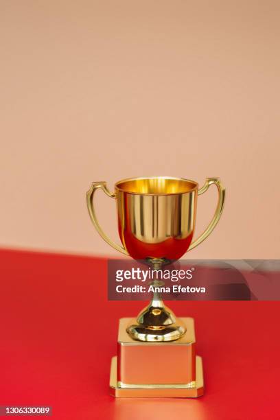 front view of metallic golden goblet on red table near beige wall. goal achievement concept - trophy wall stock pictures, royalty-free photos & images