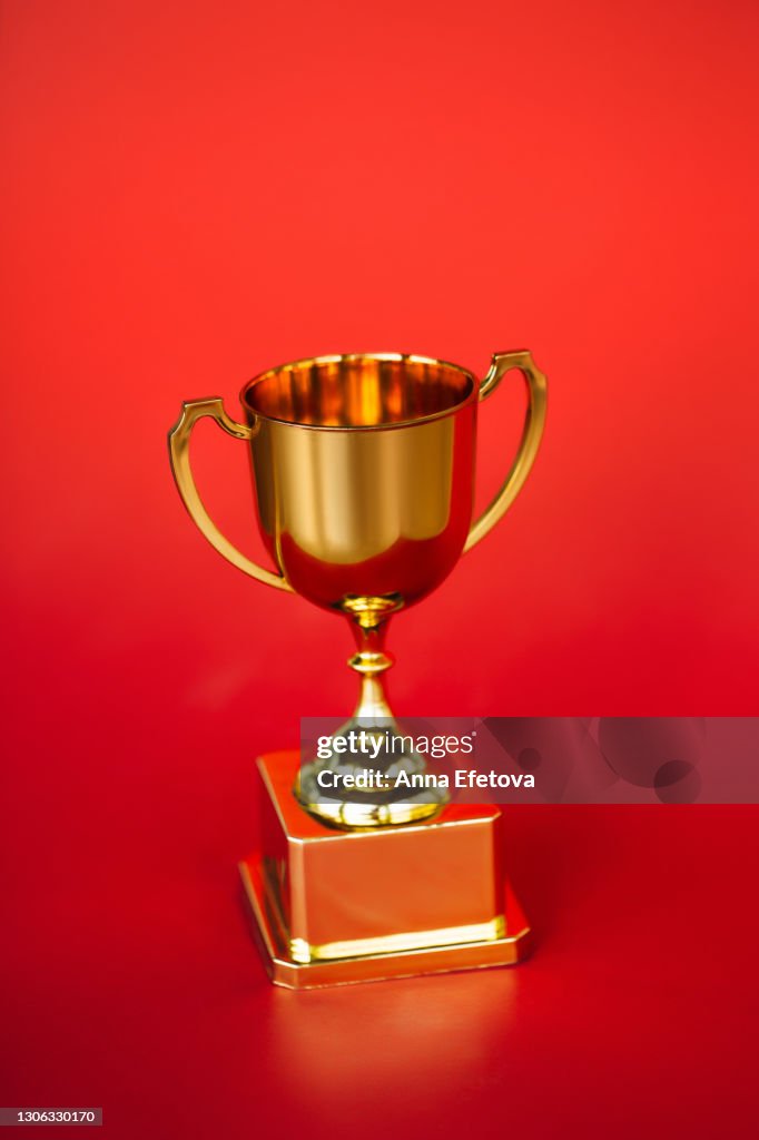 Front view of metallic golden goblet on bright red background. Goal achievement concept