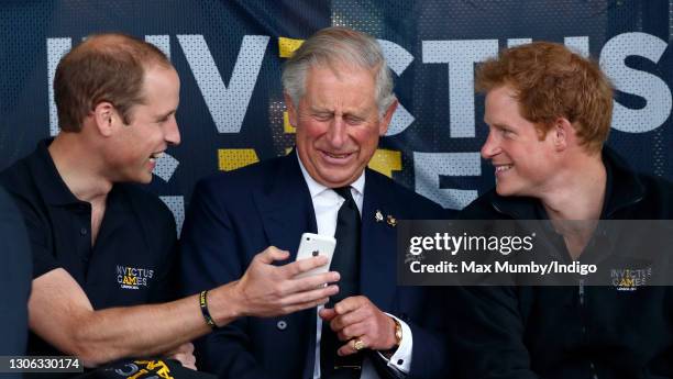 Prince William, Duke of Cambridge, Prince Charles, Prince of Wales & Prince Harry look at an Apple iPhone as they watch the athletics during the...