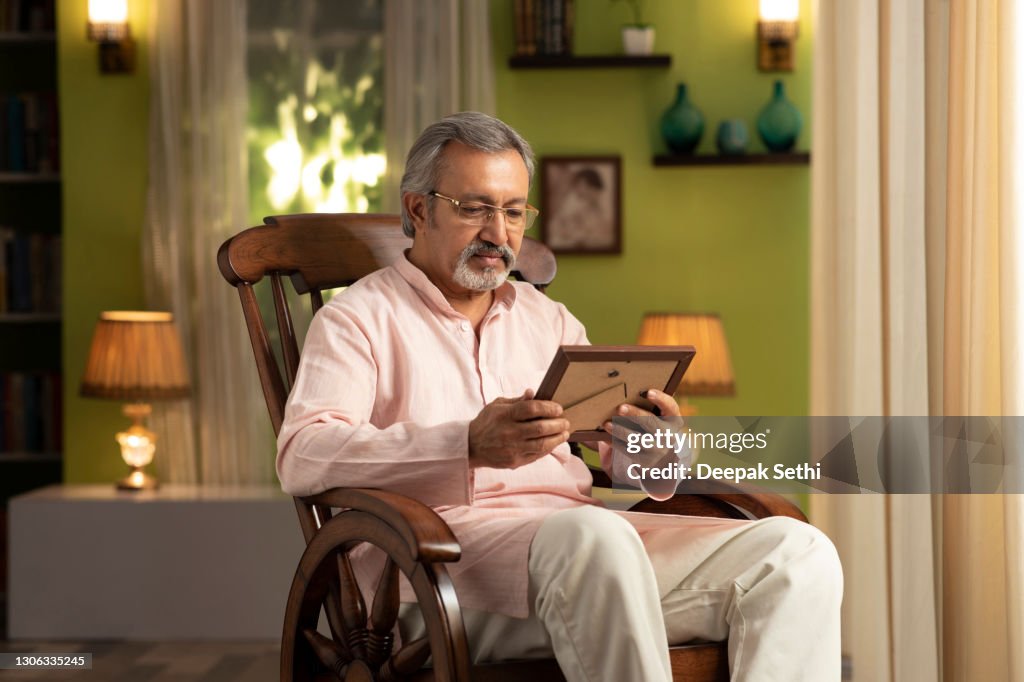 Shot of a mature man sitting on rocking chair at home:- stock photo