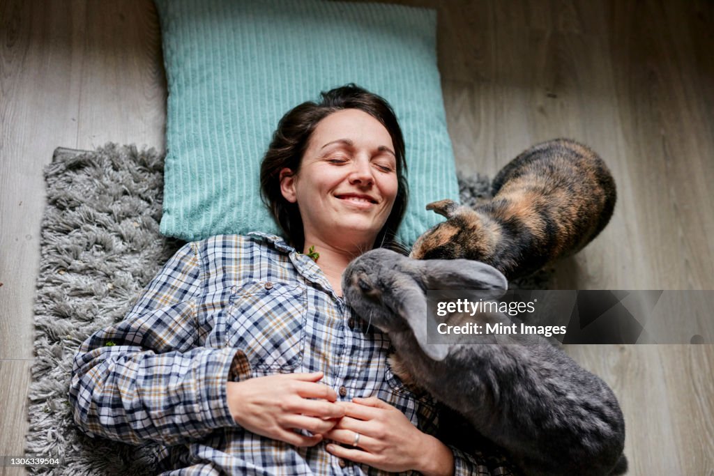 Woman lying on floor surrounded by two pet house rabbits shot from above