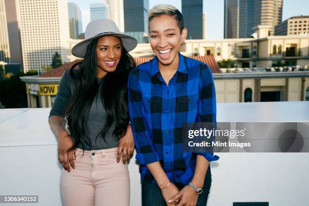 two young women on a rooftop posing for photographs, city skyline background. - straw boater hat photos et images de collection