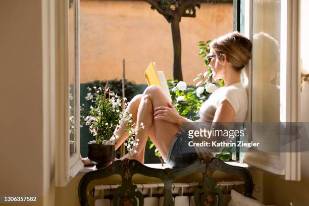 woman sitting on a windowsill, reading a book - reading stockfoto's en -beelden