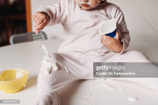 toddler over a table eating a yogurt and messing up - food stain stock-fotos und bilder