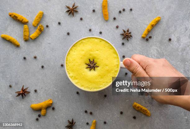 cropped hand holding turmeric latte against grey background - star anise stock pictures, royalty-free photos & images