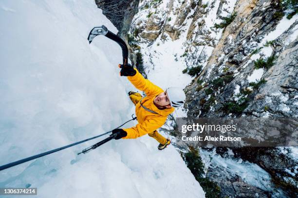 ultra wide angle shot of ice climber hanging from side of a 100 meter tall frozen waterfall with ice axes - extreme stock photos et images de collection