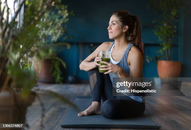 mujer en forma bebiendo un batido de desintoxicación verde en el gimnasio - relaxing fotografías e imágenes de stock