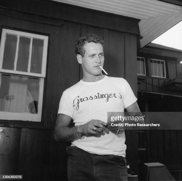 Portrait of American actor Paul Newman as he lights a cigarette, 1950s.