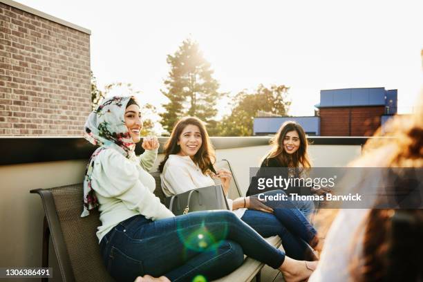 smiling and laughing female friends relaxing on rooftop deck on sunny evening - funny muslim stock pictures, royalty-free photos & images