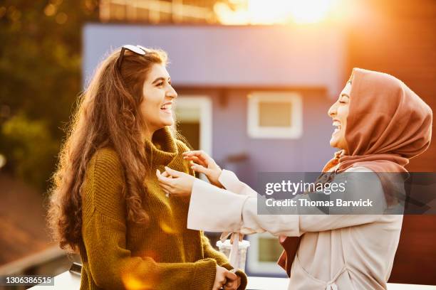 laughing sisters hanging out on rooftop deck at sunset - funny muslim stock pictures, royalty-free photos & images