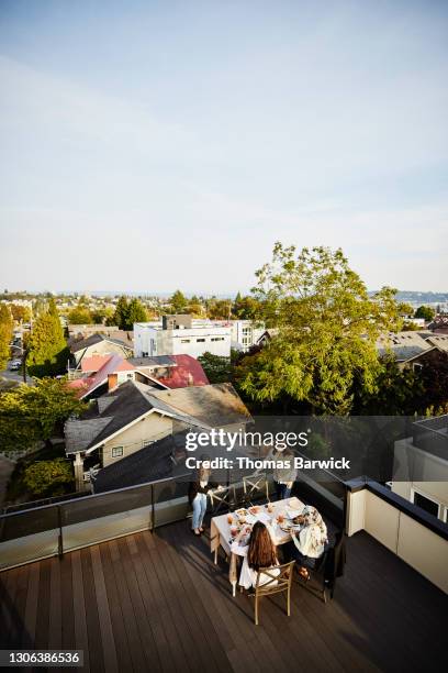 female friends sitting down for dinner on rooftop deck on sunny evening - rooftop dining foto e immagini stock