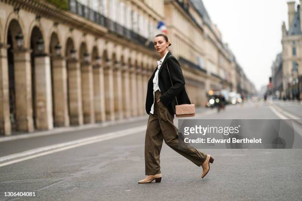 Olesya Senchenko wears a green wool oversize blazer jacket, a white long shirt, khaki pants, a pink quilted Chanel leather bag, beige pointy boots...