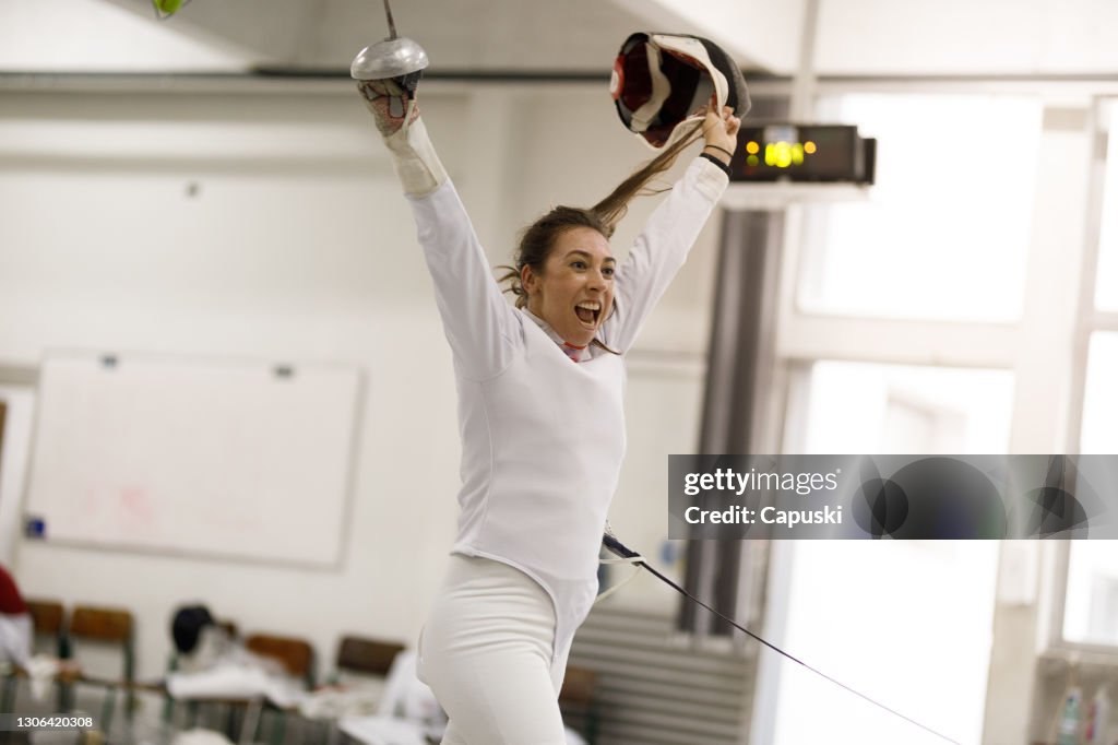Female fencer athlete with sword up celebrating a victory