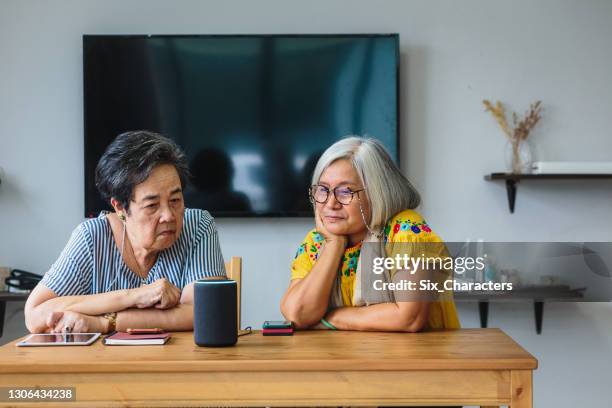 zwei asiatische seniorinnen mit smarten lautsprechern im wohnzimmer zu hause - assisted living stock-fotos und bilder