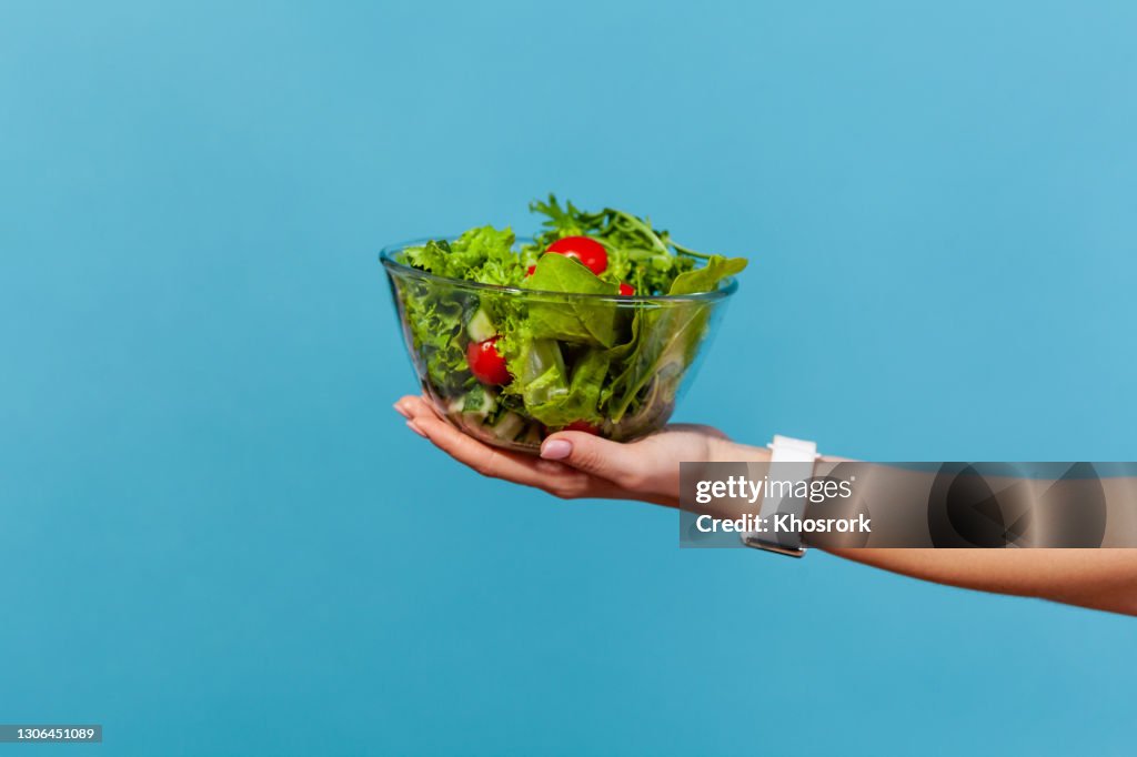 Close up female hand holding big glass bowl with green salad from fresh red tomatoes and lettuce leaves, organic nutrition, healthy eating, detox diet