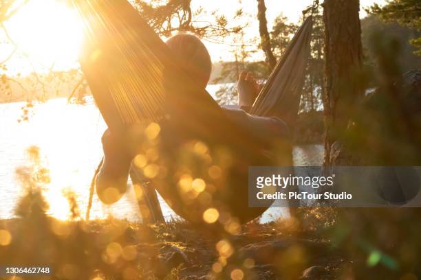 senior adult woman reading book in hammock near by lake - finland stock pictures, royalty-free photos & images