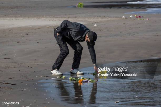 Man places flowers for the victims of the 2011 Tohoku earthquake and tsunami on a beach on March 11, 2021 in Iwaki, Japan. Japan will today observe...