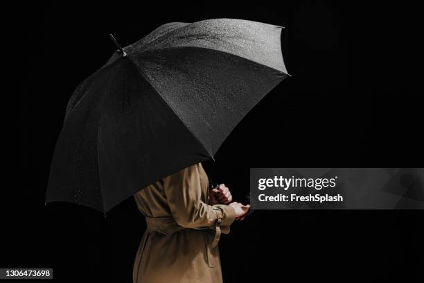anonym kvinna klädd i en regnrock som håller ett öppet svart paraply (studio shot) - regnkläder bildbanksfoton och bilder