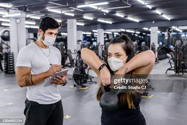 trainer taking notes on tablet during evaluation of active student with facial mask - gym reopening stock pictures, royalty-free photos & images