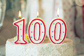 Birthday candle as number one hundred on top of sweet cake on the table, 100th birthday