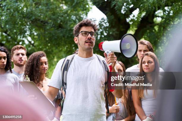 mannelijke vrijwilliger die een megafoon houdt terwijl het zich voor een groep activisten bevindt die zich in park bevinden - activists protests outside of trump tower in chicago stockfoto's en -beelden