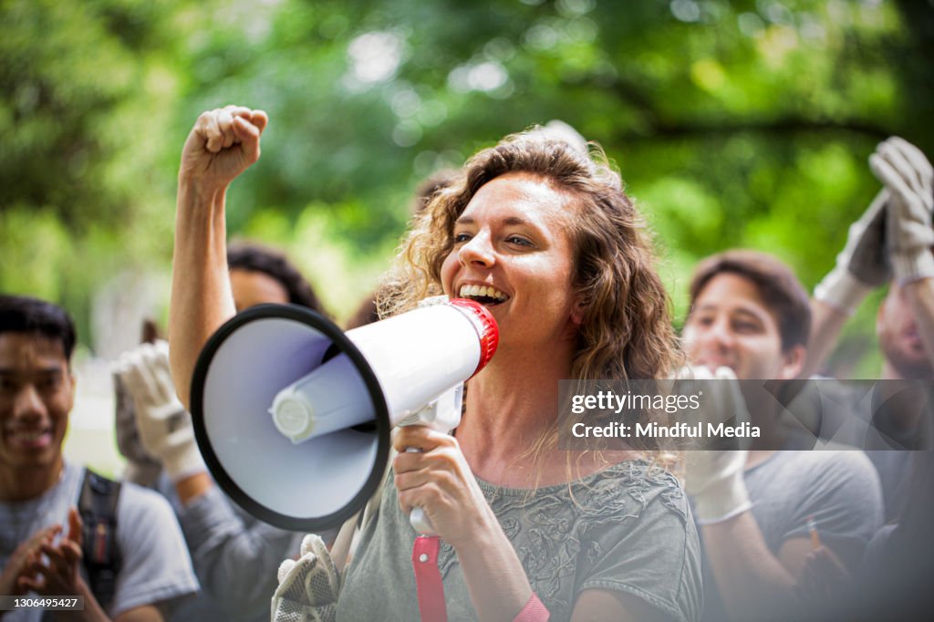 Jovem ativista segurando megafone e fazendo um discurso com o punho para cima durante evento de limpeza de lixo