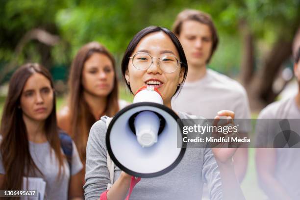 young female volunteer talking on megaphone in park - asian activist stock pictures, royalty-free photos & images