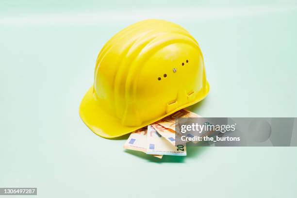 still life of a yellow construction helmet and euro banknotes on green background - bonus pay stock pictures, royalty-free photos & images