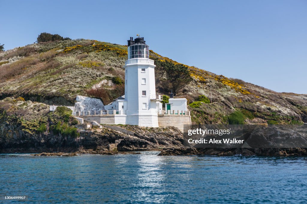 White lighthouse with rocks and green fields in idyllic location
