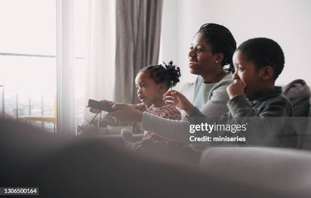 super mom: a young mother and her boy and a girl spending quality time together at home - family watching television stock pictures, royalty-free photos & images