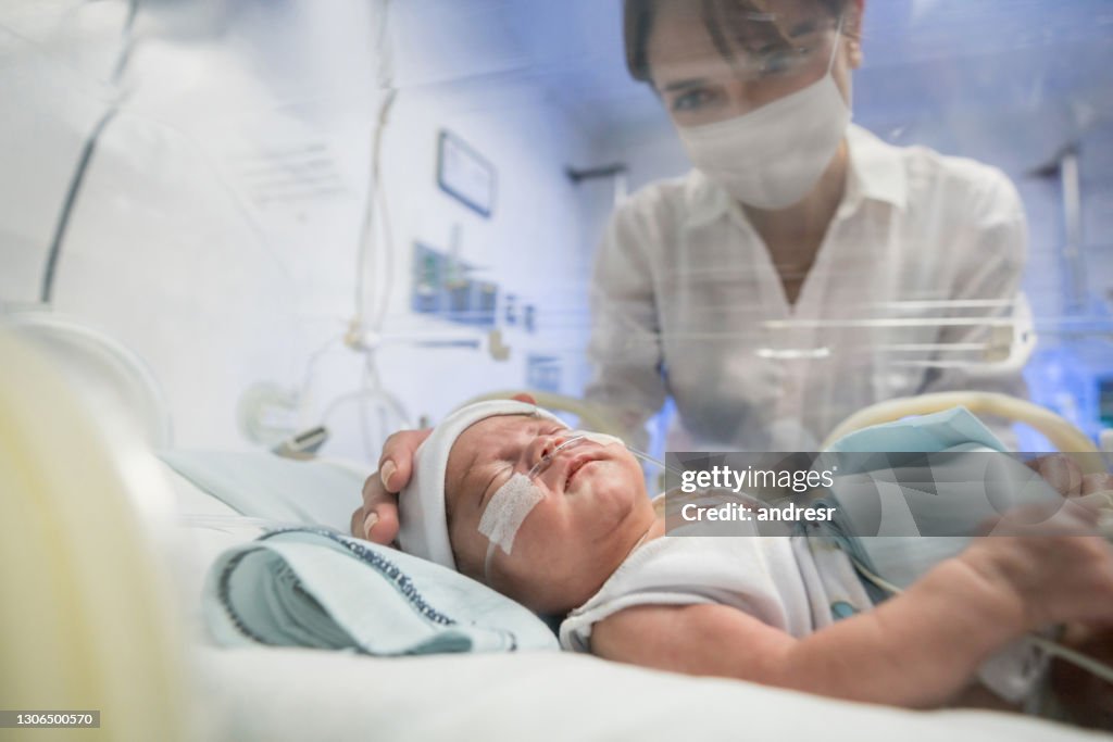 Madre amorevole che guarda il suo neonato in un'incubatrice mentre indossa una maschera facciale