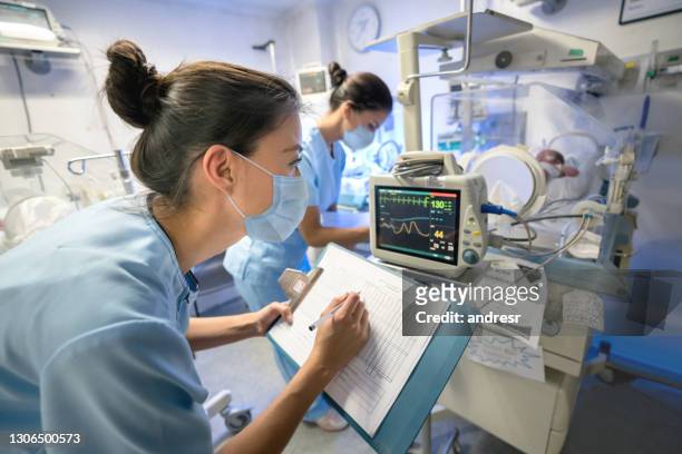 enfermera monitoreando a un recién nacido prematuro en una incubadora mientras usa una máscara facial - instrumento médico fotografías e imágenes de stock