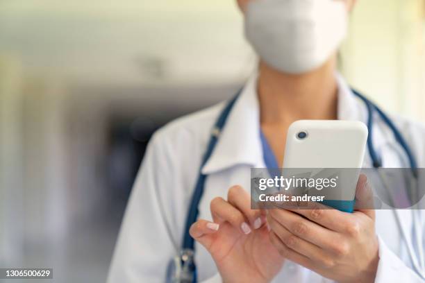 doctor using a cell phone at the hospital wearing a facemask - n95 face mask medical stock pictures, royalty-free photos & images