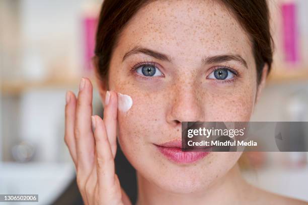 smiling young woman applying cream on her face - spreading imagens e fotografias de stock