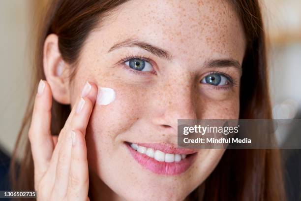 mujer sonriente aplicando crema en su cara - crema facial fotografías e imágenes de stock