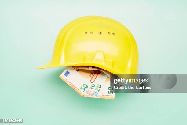still life of a yellow construction helmet and euro banknotes on green background - euroscheine stock-fotos und bilder
