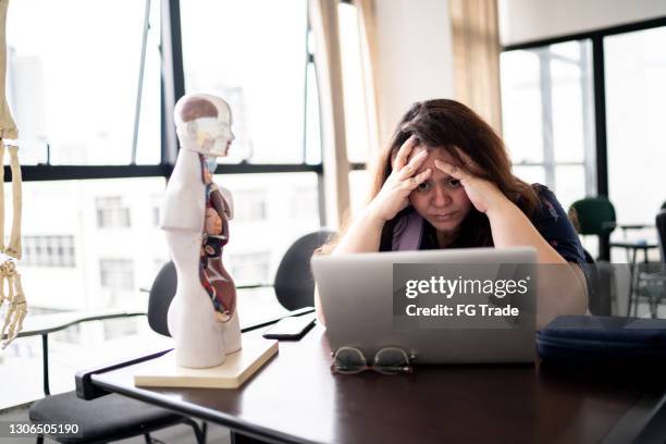 displeased teacher working using laptop in the classroom - overworked teacher stock pictures, royalty-free photos & images