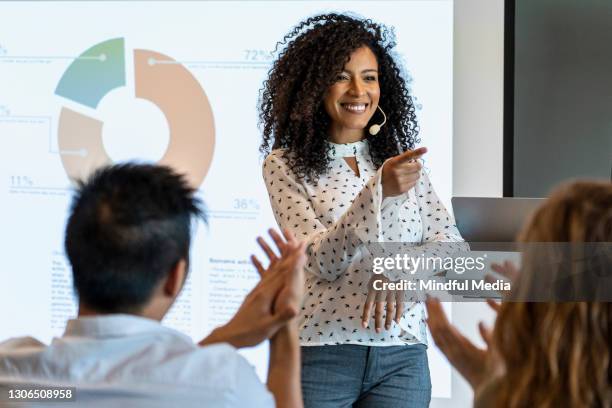 jovem empresária sorridente fazendo apresentação para seus colegas em sala de diretoria - reunião de equipe - fotografias e filmes do acervo