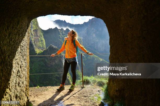 portrait of attractive young woman standing on a mountain trail while hiking in madeira island, view out of a man made tunnel, atlantic ocean, portugal - funchal stock pictures, royalty-free photos & images