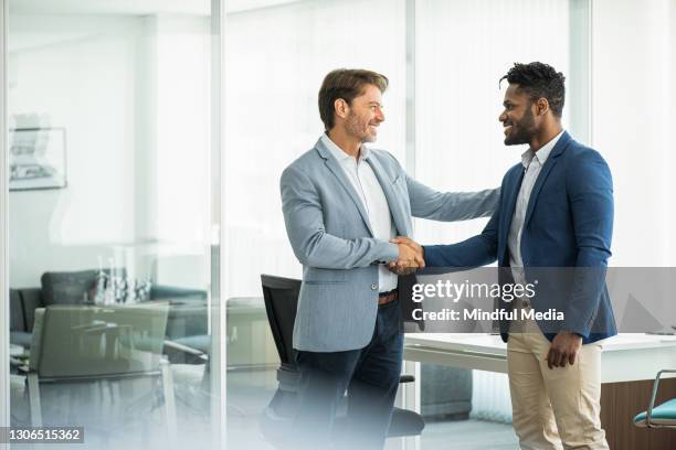 smiling businessmen shaking hands in board room - black men shaking stock pictures, royalty-free photos & images