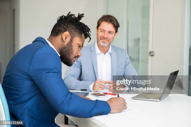 mature man looking at businessman signing document in office - man signing paper stock pictures, royalty-free photos & images