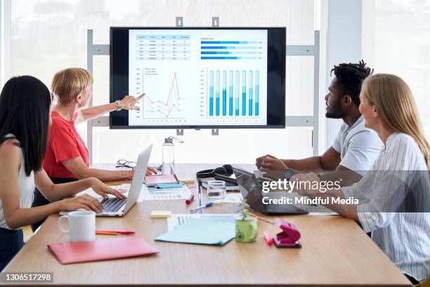 businesswoman discussing financial graphic on screen with her colleagues in office - data sharing stock pictures, royalty-free photos & images