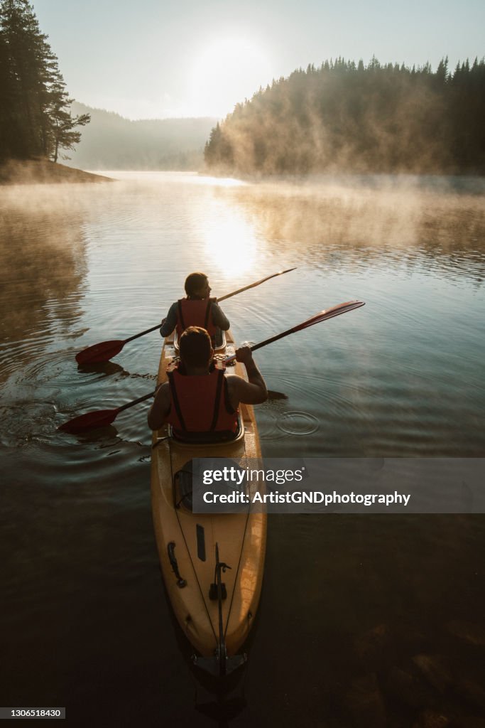 Young couple paddling kayak across the mountain lake.