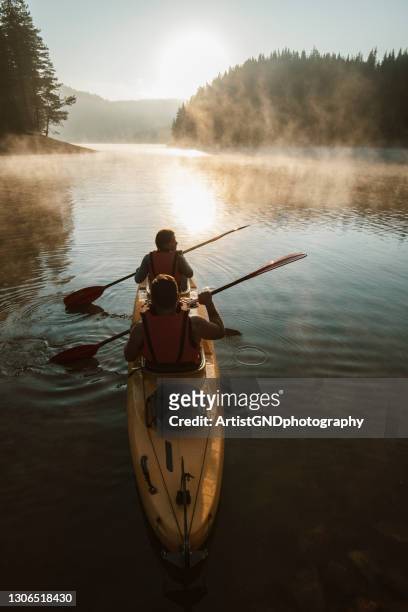 young couple paddling kayak across the mountain lake. - kayak stock pictures, royalty-free photos & images