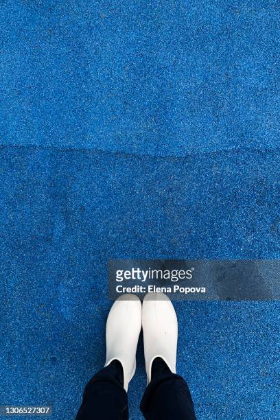 woman in white rubber boots standing on the blue jogging track - feet selfie woman stockfoto's en -beelden