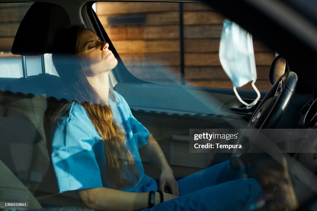 A female nurse is resting inside her car.