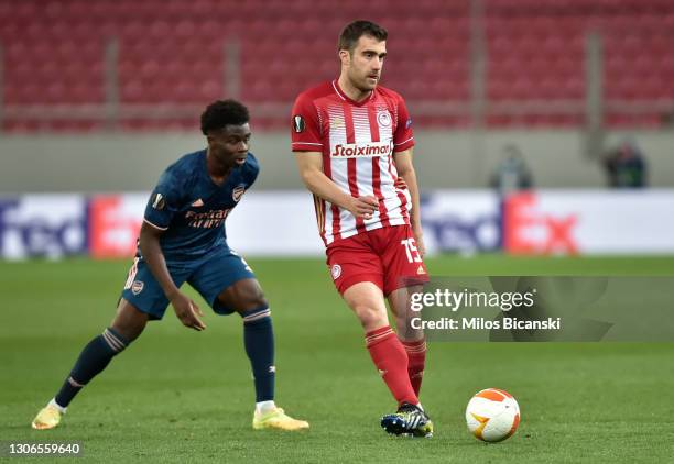 Sokratis Papastathopoulos of Olympiakos is challenged by Bukayo Saka of Arsenal during the UEFA Europa League Round of 16 First Leg match between...