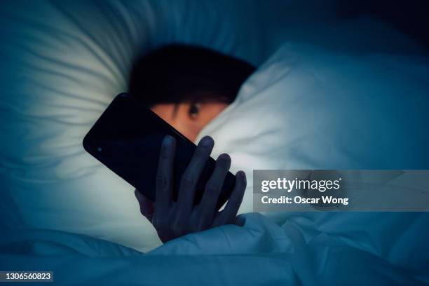 woman hiding under the blanketed and using smart phone at late night on bed - 嫌がらせ ストックフォトと画像